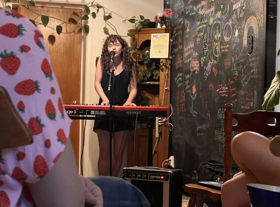 A person plays piano and sings in a room of people.